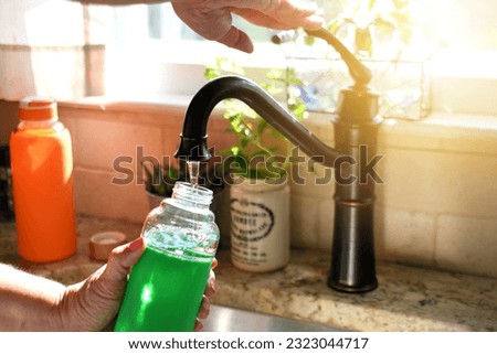 Woman filling reusable eco-friendly glass water bottle at tap, environmentally friendly container Royalty-Free Stock Photo #2323044717