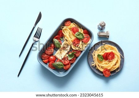 Baking dish with tasty tomatoes, feta cheese and pasta on blue background