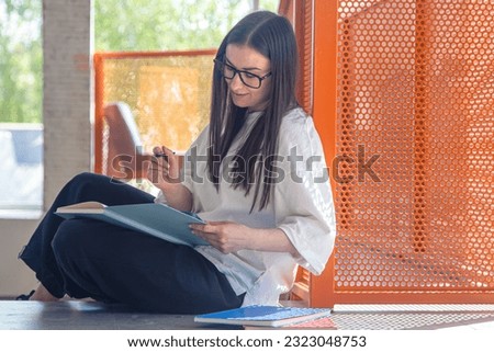 Young woman with notebooks sits in a modern interior, the concept of study and teaching.