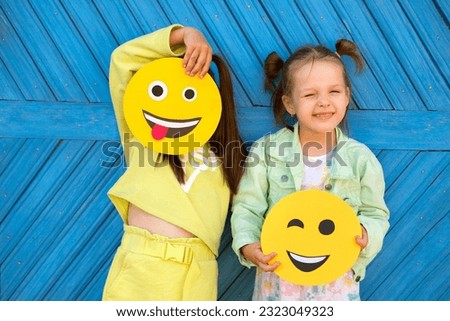 Humorous funny girls hold various funny smile faces and make faces standing at the blue wall
