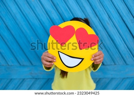 A human holds a romantic emoticon in love with eyes in the shape of hearts on a blue background