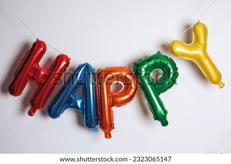 Inflatable balloons made of colored foil in the form of letters. Multicolored inscription happy on light background. Front view