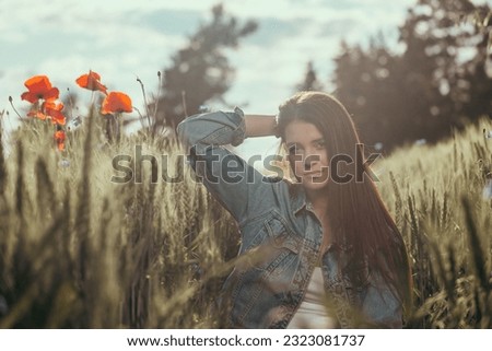 Atractive long haired  brunette girl dressed in blue jeans is posing in a cornfield. The photo is edited as a cinema photo. Horizontally. 