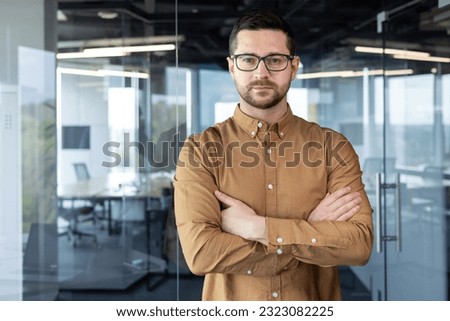 Portrait of a young self-confident businessman, executive director, founder standing in an office building. He crosses his arms on his chest and looks seriously into the camera. Royalty-Free Stock Photo #2323082225
