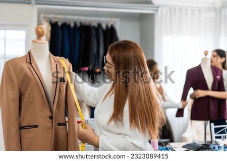 Diverse women fashion designer work design clothes in tailoring atelier. Attractive young female tailor dressmaker team feel happy and enjoy design new pattern collection of clothes in workshop store.