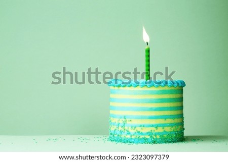 Green and blue striped birthday cake with one celebration birthday candle against a plain green background