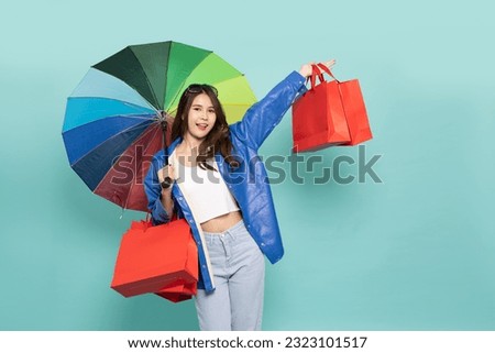Young Asian woman wearing raincoat and holding rainbow umbrella and shopping bag isolated on green background, Shopping in the rainy season concept