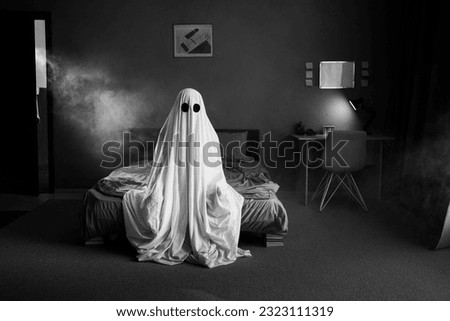 Ghost in a white sheet sits on a bed in bedroom in smoke, black and white photo. Halloween concept. Copy space Royalty-Free Stock Photo #2323111319