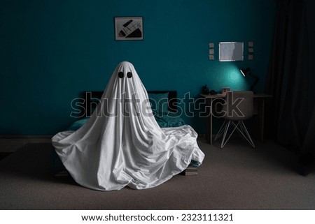White ghost sitting on bed in bedroom, halloween concept. Place for text Royalty-Free Stock Photo #2323111321