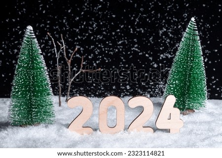 Creative 2024 New Year's card. A composition of wooden figures of the year 2024 in a snowy forest during a snowfall at night. Waiting for a miracle