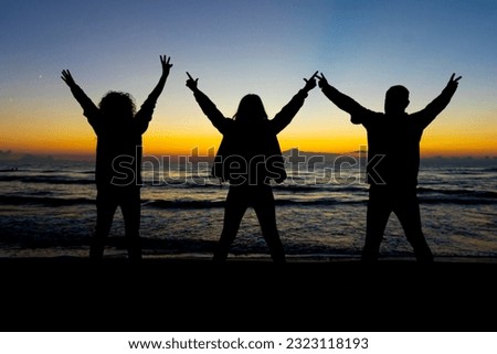 silhouette of 3 people raising their arms on the beach