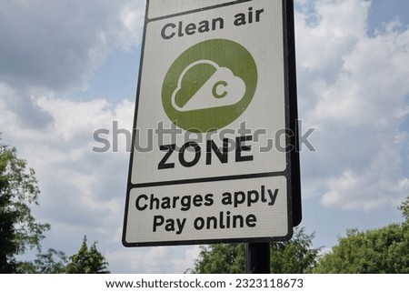 View of a generic clean air zone congestion charge road sign again a sky with clouds and green leafy trees -  congestion charges for polluting vehicles are being adopted in cities around the world Royalty-Free Stock Photo #2323118673