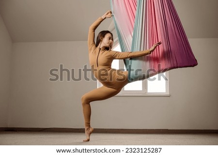 Caucasian woman doing air yoga exercises with fabric indoors