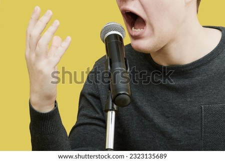 Young man's mouth wide open in front of a microphone. Public emotion, singer's emotional performance, emotional speech, negative emotion in public Royalty-Free Stock Photo #2323135689