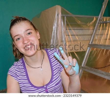 young girl makes the sign of win while she is painting a room