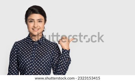 Portrait of happy young Indian woman isolated on grey studio background show point at blank empty advertising copy space. Smiling mixed race female recommend promotion offer or sale discount.