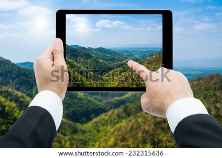Businessman hands tablet taking pictures View green mountains and a blue sky