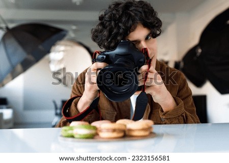 Food photographer caucasian man taking photos of delicious sweets macarons at photo studio, using digital camera and professional lighting equipment