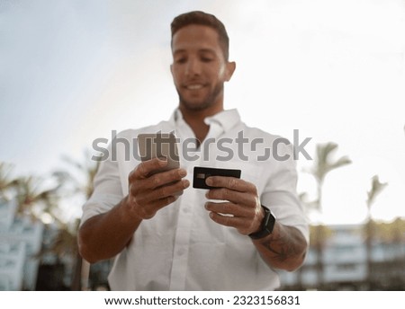 Young businessman with smartphone and credit card in hands standing outdoors, man entrepreneur making online shopping or money transfers, selective focus