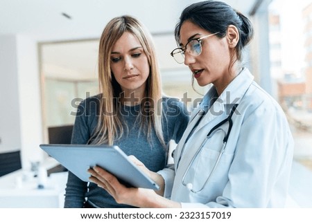 Shot of beautiful female doctor talking while explaining medical treatment with digital tablet to patient in the consultation. Royalty-Free Stock Photo #2323157019