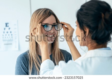 Shot of female doctor choosing while proving eyeglasses to mature beautiful patient in medical consultation.