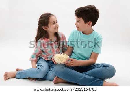 Happy preteen boy and girl eating popcorn, smiling talking to each other, isolated on white studio background. Happy kids. Family relationships. Loving caring brother and sister. Son and daughter