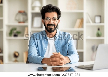 Millennial Freelancer. Portrait Of Young Indian Man Sitting At Desk With Laptop In Home Office, Enjoying Remote Work Opportunities, Eastern Guy In Eyeglasses Smiling And Looking At Camera Royalty-Free Stock Photo #2323171331