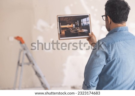 Man in glasses looking at picture with loft-style interior design standing in unfinished room against ladder and shabby wall home owner ready for renovation in apartment