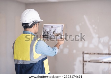Experienced engineer imagining finished renovation of living room man in hardhat and vest looking at picture of Scandinavian interior design in hands standing against shabby wall