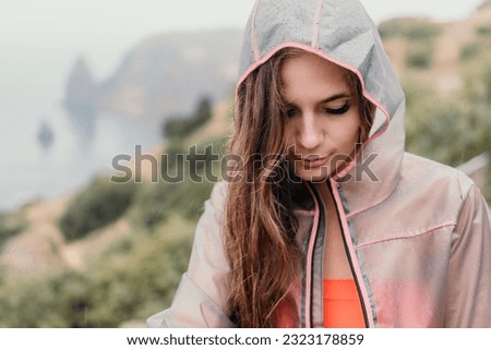 Woman rain umbrella. Happy woman portrait wearing a raincoat with transparent umbrella outdoors on rainy day in park near sea. Girl on the nature on rainy overcast day.