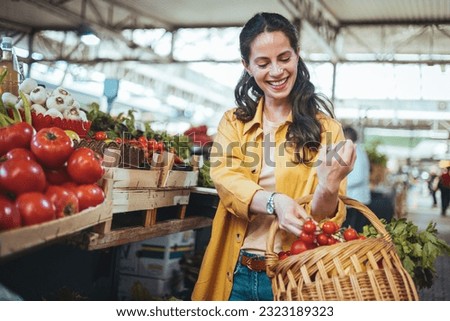 View at young woman buying vegetables at the market. A woman shops in a local outdoor agriculture market with fresh, organic local fruits and vegetables. She smiles as she compares different vegetable