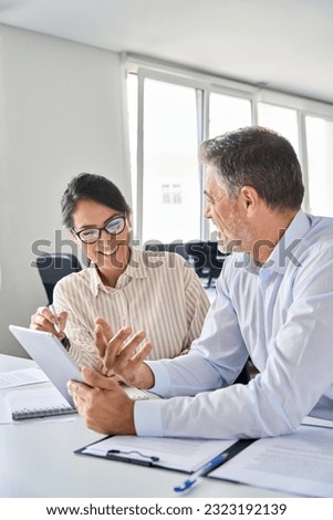Two happy professional business people team Asian woman and Latin man workers working using digital tablet discussing financial marketing strategy at corporate office meeting, vertical. Royalty-Free Stock Photo #2323192139