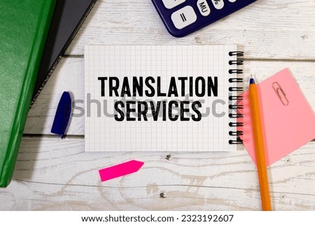 On a light background, gold-framed glasses, a flower in a pot, a green notebook, a red pen and a brown notebook with the text TRANSLATION SERVICES. Business concept Royalty-Free Stock Photo #2323192607