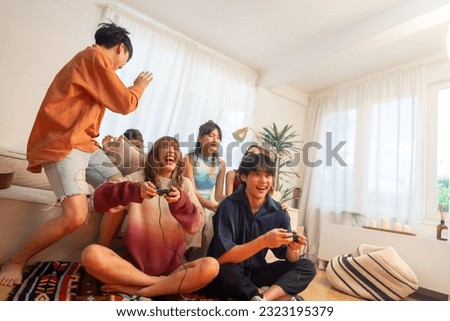 Group of Young Asian man and woman playing video games together in living room at home. Happy people friends enjoy and fun indoor activity lifestyle spending time together on holiday vacation. Royalty-Free Stock Photo #2323195379
