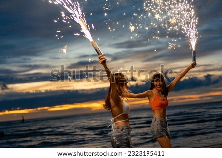 Young Asian woman friends playing sparklers firework together at tropical island beach at summer sunset. Attractive girl enjoy and fun outdoor lifestyle beach party on holiday travel vacation. Royalty-Free Stock Photo #2323195411