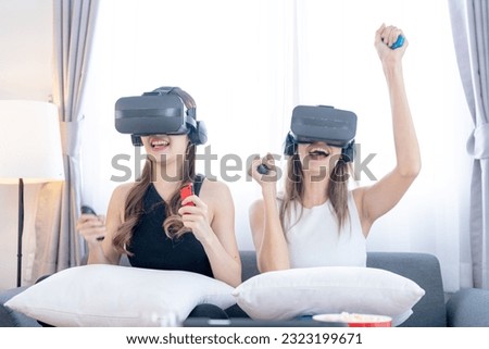 Young happy asian girls playing video games virtual reality glasses in living room. Cheerful people having fun with new trends technology. Man with hands up wearing the virtual reality goggles.