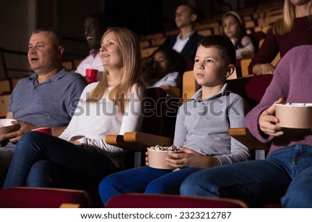 Portrait of cute tween boy visiting cinema with his family, holding popcorn and watching movie with interest
