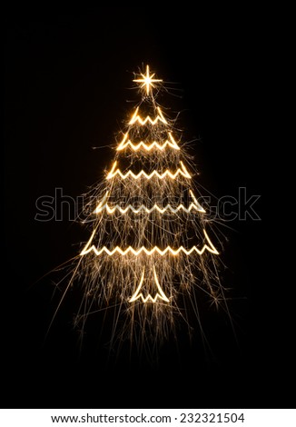 Christmas tree icon in sparks on black background.