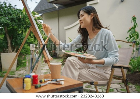 Artist concept, Female artist holding watercolor palette to painting on canvas in outdoor garden.