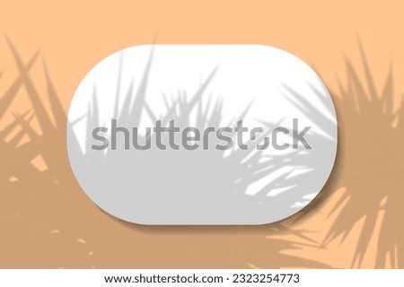 A horizontal oval sheet of white textured paper on the orange wall background. Mockup overlay with the tropical plant shadows. Natural light casts shadows from an willow branch. Horizontal