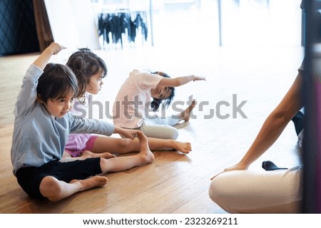 Female instructor in a gymnastics class teaching stretching to a toddler