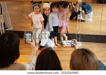 Children's mothers taking pictures of teacher and students in gymnastics class