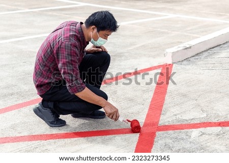 Painter is painting red color no parking symbol with paint roller at the parking floor on urban street.
