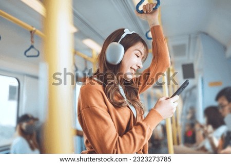 Happy young Asian woman passenger listening music via smart mobile phone in a train, Smile female wearing wireless headphones while moving in the tram, lifestyle, transportation. Royalty-Free Stock Photo #2323273785