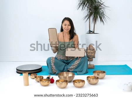 A young Asian woman sits in a lotus position near the Tibetan communal bowls. A woman holds Sadhu boards in her hands. High quality photo