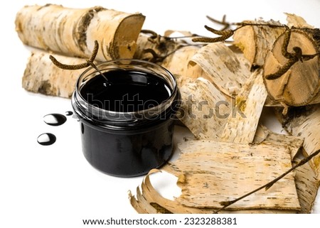 Birch tar or pitch in a jar and birch tree bark on white background. Wood tar. Liquid mineral tar from birch bark Royalty-Free Stock Photo #2323288381