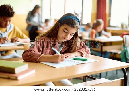 Schoolgirl writing while learning during a class in the classroom. Royalty-Free Stock Photo #2323317591