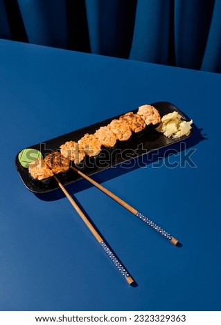 Glistening baked spicy sushi set - gunkans on a black plate, set against a deep blue curtain background with dramatic shadows. Perfect for an Asian menu.
