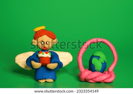 An angel figurine with an Easter cake on a green background. Next to the basket with an Easter egg in the form of the planet earth.