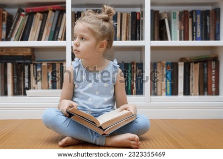Little cute girl in the glasses sitting in the front of bookshelf. Concept of education in the library